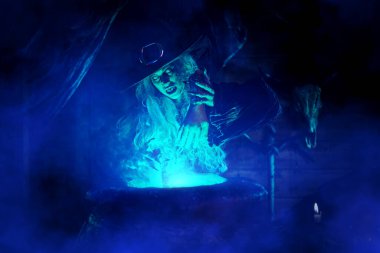 Korkunç yaşlı cadı, sihirli mavi ışıkla çevrili kazanında iksir yapıyor. Cadılar Bayramı. Korkunç hikayeler..