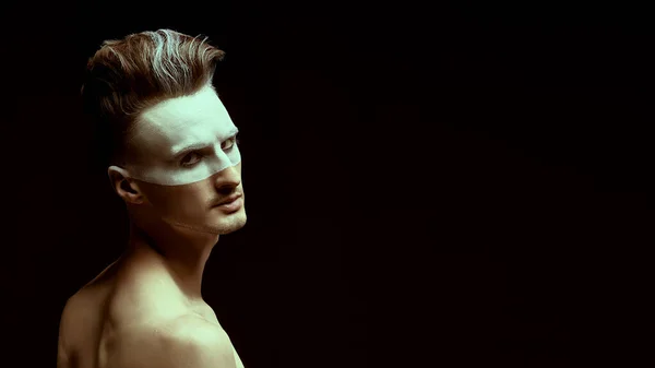 Art concept. Portrait of a brutal serious man with white paint on his face and hair on a black background. Men's beauty, fashion. Hairstyle and cosmetics.