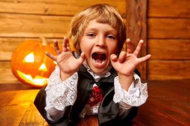 Cadılar Bayramı. Karnaval kostümü giymiş şirin bir çocuk yerde yatıyor ve parlayan bir balkabağı fenerinin arka planındaki kameraya bakıyor..