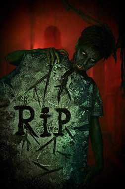 Korkunç Cadılar Bayramı. Korkunç zombi çocuk mezarlıktaki mezar taşının arkasından dikizliyor. Boşluğu kopyala.