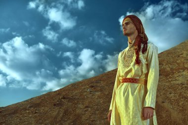 Gün batımında çölde Kızılderili kostümü giymiş yakışıklı bir gencin portresi. Erkek güzelliği, moda.