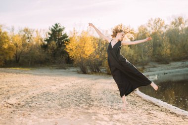 Güzel bir genç kız dışarıda siyah bir elbise içinde hareket halinde poz veriyor. Moda konsepti.