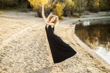 Güzel bir genç kız dışarıda siyah bir elbise içinde hareket halinde poz veriyor. Moda konsepti.