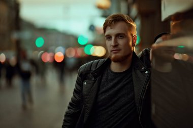 Büyük bir şehirde akşam hayatı. Modern genç adam şehir caddesinde yürüyor akşam ışıklarıyla aydınlatılıyor.