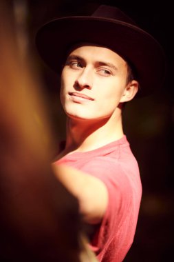 Güneşli sonbahar ormanlarında şapkalı yakışıklı bir gencin yakın plan portresi. Erkek güzeli.. 