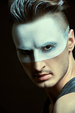 Yüzünde beyaz boya, siyah arka planda ışık olan yakışıklı bir gencin sanat portresi. Erkek güzeli, moda. Saç stili ve kozmetik.