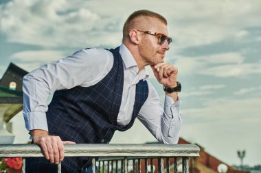 Zarif klasik takım elbiseli mutlu ve olgun bir adam yaz terasında dinleniyor. Erkek modası. Optik, erkekler için güneş gözlüğü. Yaz tatili.