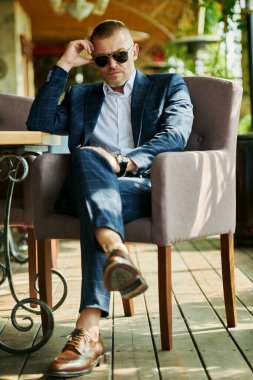 Zarif klasik takım elbiseli yakışıklı olgun bir adam yaz terasında dinleniyor. Erkek modası. Optik, erkekler için güneş gözlüğü. Yaz tatili.