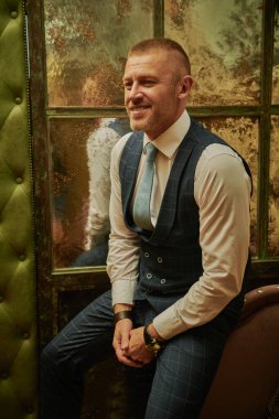 Lüks bir dairede kapının yanında oturan zarif bir takım elbiseli, olgun, yakışıklı bir adamın portresi. Erkek güzelliği, moda.