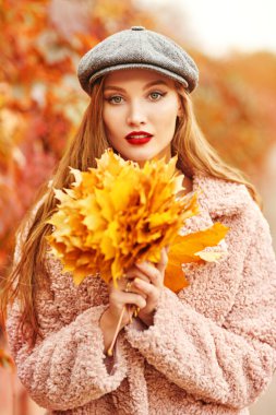 Mutlu sonbahar havası. Güz parkında elinde bir buket sarı akçaağaç yaprağıyla güzel genç bir kadın yürüyor.. 