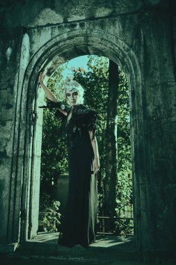 Güzel gri saçlı ve zengin siyah elbiseli aristokrat bir dul kadın mezarlıktaki bir mahzende üzgün duruyor. Kara Dul. Gizemciliğin atmosferi. Cadılar Bayramı.
