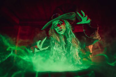 Korkunç yaşlı cadı, sihirli yeşil ışıkla çevrili kazanında iksir yapıyor. Cadılar Bayramı. Korkunç hikayeler..