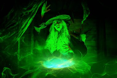 Korkunç yaşlı cadı, sihirli yeşil ışıkla çevrili kazanında iksir yapıyor. Cadılar Bayramı. Korkunç hikayeler..