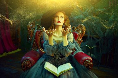 Eski şatoda bir büyü kitabıyla koltukta oturan şapkalı ve güzel elbiseli çekici bir cadı portresi. Cadılar Bayramı. Kutlama.