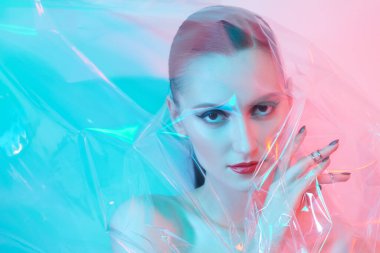 Sanat güzellik konsepti. Güzel esmer bir kızın portresi şeffaf bir film vasıtasıyla narin mavi ve pembe ışıkla. Makyaj ve kozmetik.