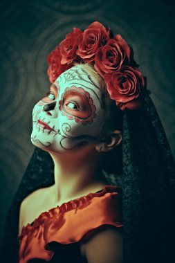 Arka planda Calavera Catrina kostümlü bir çocuk portresi. Kafatası şekeri makyajlı küçük bir kız. Cadılar Bayramı. Dia de los muertos. Ölülerin Günü.