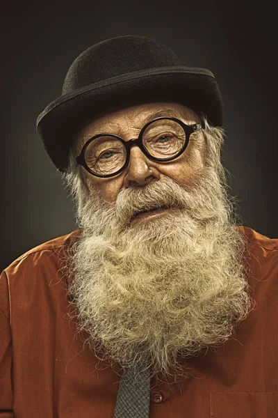 Portrait of an old-fashioned old man with a white beard in a bowler hat and round glasses. Old age. Black background.