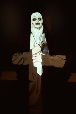 Korkunç şeytani rahibe, karanlık bir odada, ışık altında haç şeklinde dua ediyor. Korku ve Cadılar Bayramı.