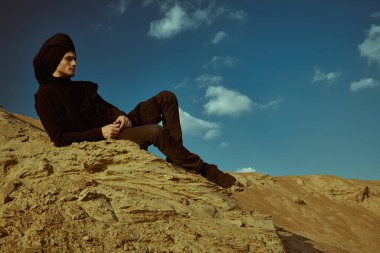 Maceralar, özgürlük ruhu. Siyah elbiseli ve başında siyah sarık olan cesur genç bir adam çölde oturuyor ve düşünceli görünüyor.. 