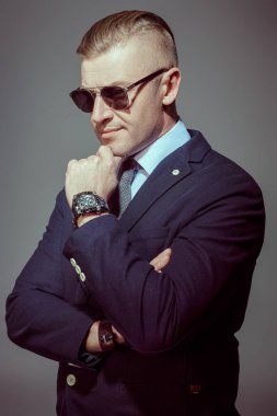 Gri arka planda güneş gözlüğü ve takım elbiseli saygıdeğer olgun bir adamın portresi. İş adamı portresi. Boşluğu kopyala.