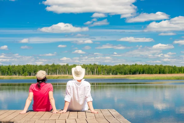 木製の桟橋の上に座って美しい湖を楽しむ若いカップル — ストック写真