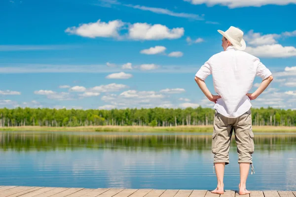 美しい湖の背景に木製の桟橋に素足で完全な長さの男 — ストック写真