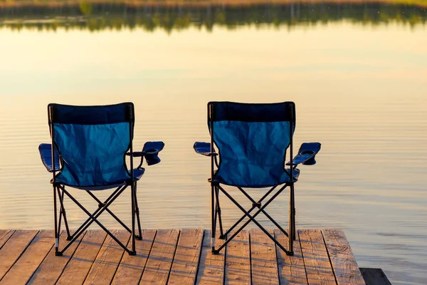 two chairs without people on a wooden pier near the lake at dawn