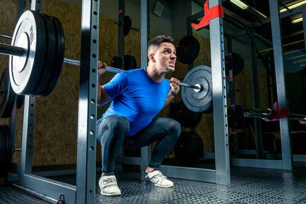 bodybuilder in a blue T-shirt raises a bar weighing 60 kg in the gym