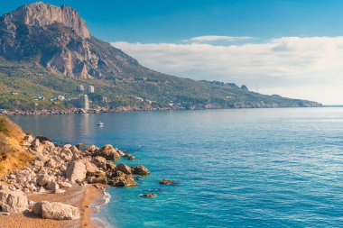 Yüksek dağlar, kayalar ve güneşli bir mavi sakin deniz