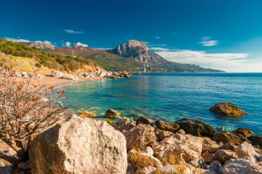 Kayalık sahil, dağ ve güneşli bir deniz manzarası