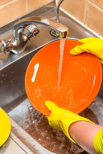 female hands washing a plate in the kitchen sink under running water