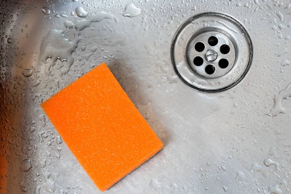 drain stainless kitchen sink and orange sponge closeup