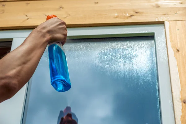 Washing window, closeup of spray cleaner in male hand on window — Stock Photo, Image