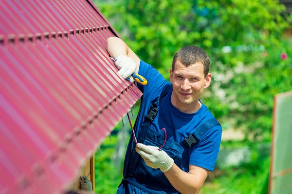 Een jonge man herstelt het dak van het huis in overall met een te — Stockfoto