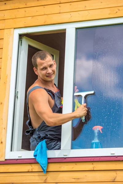 Portret van een man in overall met tools wast een venster in de — Stockfoto