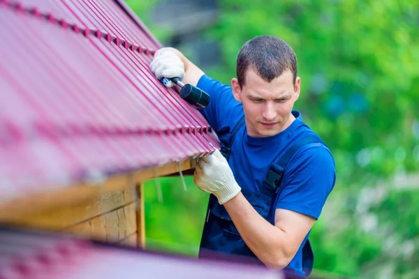 Een man met een hamer herstelt het dak van een huis, schieten buitengedeel — Stockfoto