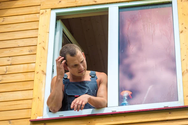 Nachdenklicher Mann in Latzhose denkt über Fensterputzen nach — Stockfoto