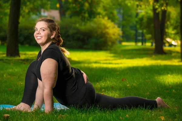 Young flexible and beautiful woman plus size in the park on the — Stockfoto