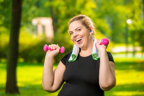 Horizontal portrait of a happy plump woman with dumbbells in the — Stock Photo, Image