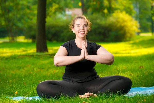 Plus size woman posing in park performing exercises in lotus pos — Stock Photo, Image