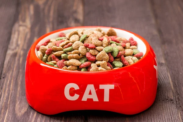 Primer plano tazón de gato rojo con comida seca en el suelo en casa — Foto de Stock