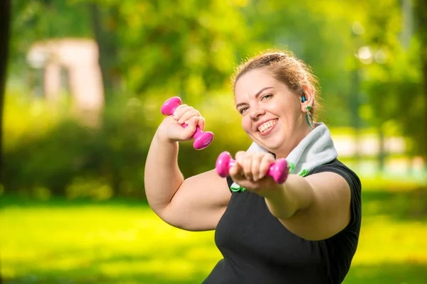 Portrait of smiling plus size woman with dumbbells in the park d — Stock Photo, Image