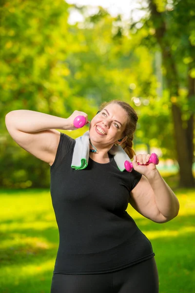 Vertical portrait of a happy plus-size model with dumbbells duri — Stock Photo, Image