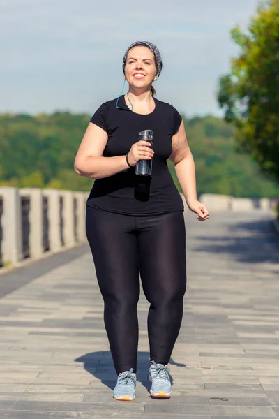 Plus size donna attiva con una bottiglia d'acqua durante una mattina j — Foto Stock