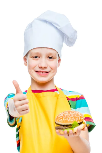 Niño feliz cocinero en gorra y delantal con hamburguesa de queso con chuleta —  Fotos de Stock