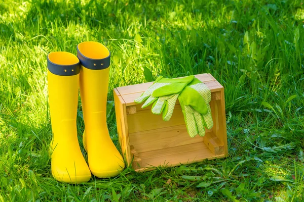 wooden box, green gloves and yellow rubber boots on lush grass i