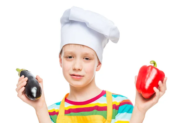 Retrato de un niño en un sombrero de cocina con pimienta y berenjena en un —  Fotos de Stock