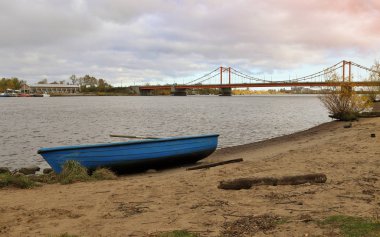 Arkhangelsk. Autumn day on the Bank of the Northern Dvina river opposite Solombala. Golden autumn leaves on eve. View of the cable-stayed bridge across the river kuznechiha. boat on the shore. The sun's rays through the clouds.  clipart