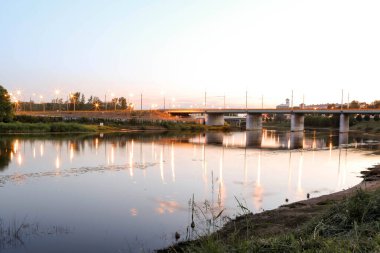 Yaroslavl. Kotorosl nehrinin kıyısında sıcak bir akşam. Kotorosl nehri üzerindeki köprüler gün batımı ve akşam ışıklarının arka planında. Suyu sakinleştirmek için yansıtma. Doğanın yansıması.