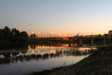 Yaroslavl. Kotorosl nehrinin kıyısında sıcak bir akşam. Kotorosl nehri üzerindeki köprüler gün batımı ve akşam ışıklarının arka planında. Suyu sakinleştirmek için yansıtma. Doğanın yansıması.